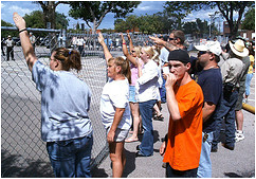 A picture showing a gathering behind a fence on a sunny day in the south of America , some of the members of the crowd are using the Nazi salute to attack a black rights march that is occuring on the other side of the fence